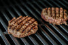 Two grilled Ostrich burger patties cooking on a grill