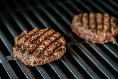 Two grilled Ostrich burger patties cooking on a grill