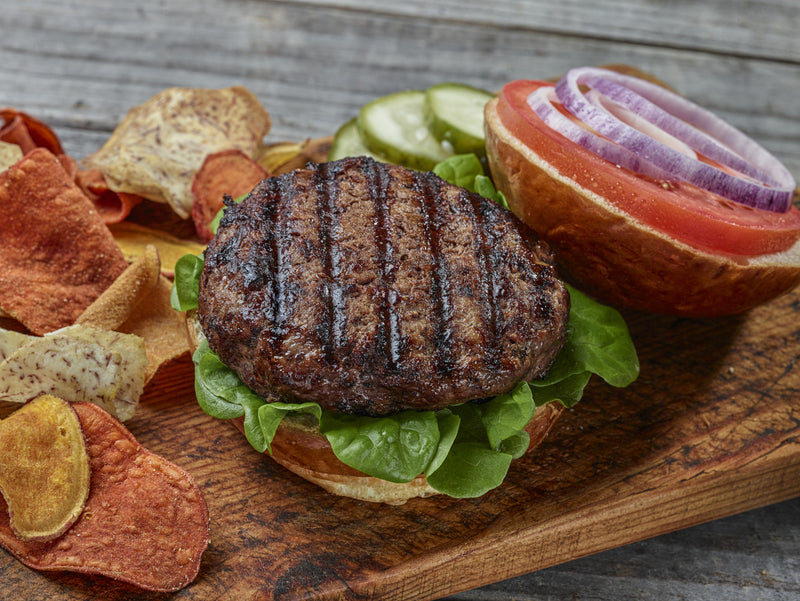 Picture of a delicious grilled Ostrich Burger patty on a bun surrounded by condiments. 