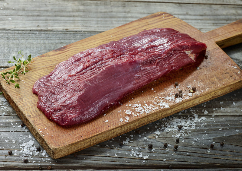 A raw Ostrich Steak Inside Strip Filet  being prepared on a cutting board.
